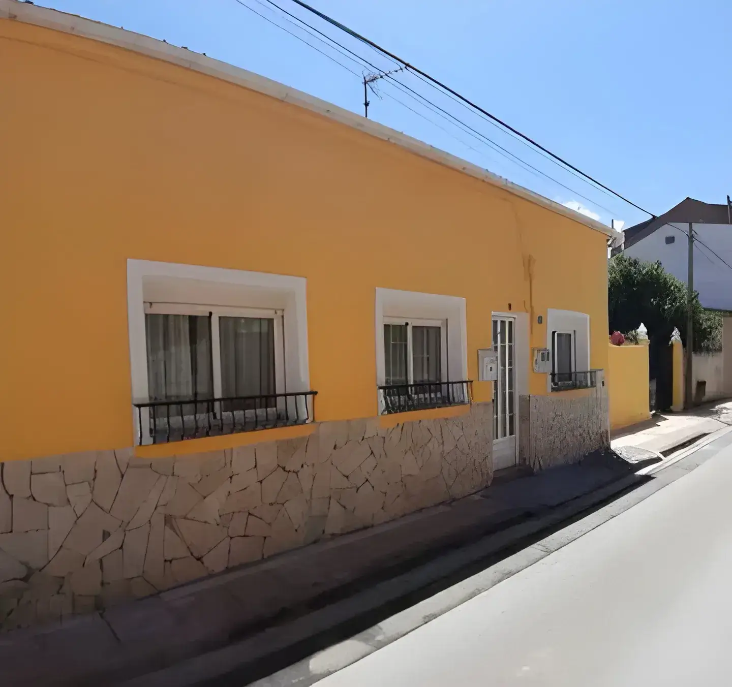 Los Pintores Albacete Fachada de casa tradicional pintada en color amarillo con zócalo de piedra
